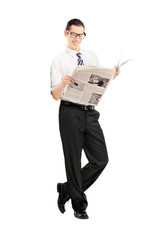 Smiling businessman leaning against wall and reading a newspaper