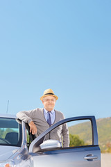 Confident mature gentleman with hat posing next to his car