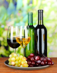 Wine bottles and glasses of wine on tray, on bright background