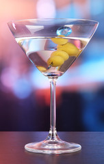 Martini with green olives on table in bar