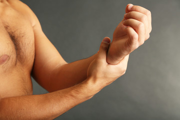 Young man with hand pain on grey background