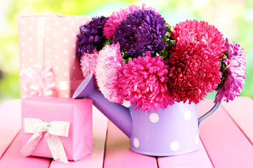 Gifts and flowers in watering can, on nature background