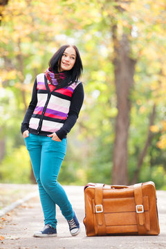 Brunette girl holding suitcase at autumn alley in the park