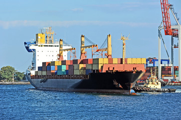 Tugboat assisting container cargo ship to harbor quayside