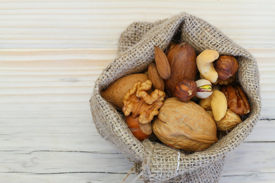 Selection of nuts in jute bag on wooden surface with copy space