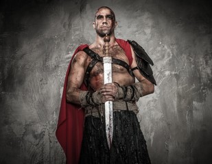 Wounded gladiator holding sword covered in blood with both hands