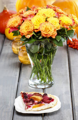 Piece of cake and huge bouquet of orange roses on wooden table.