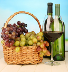 Ripe grapes in wicker basket, bottles and glass of wine,