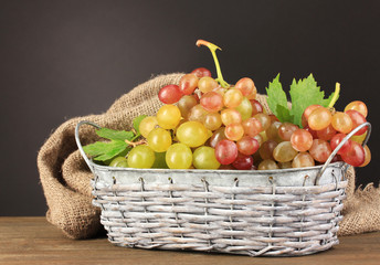 Ripe sweet grape in basket on wooden table, on grey background