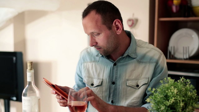 Young man with tablet computer drinking wine at home