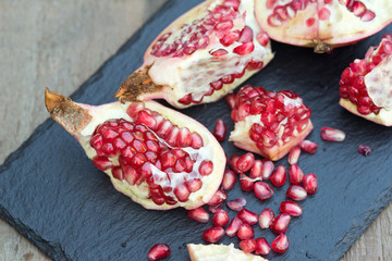 Fresh open pomegranate with seeds out on slate base and wooden b