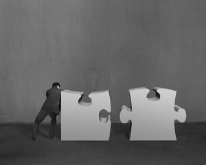 Businessman push two heavy puzzles together in concrete wall bac