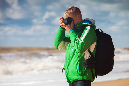 Young man with camera makes sea snapshot