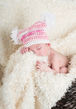 Beautiful newborn baby wearing a pink hat with white pom poms