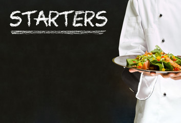 Chef with chalk starters sign on blackboard background