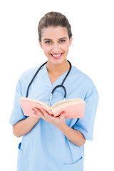 Happy brown haired nurse in blue scrubs holding a book