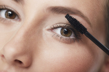 Portrait of young woman applying mascara, close up