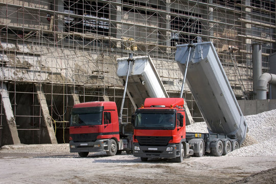 Two big red trucks delivering gravel on construction site