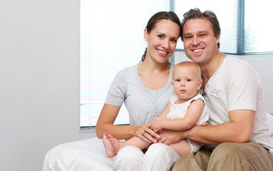 Obraz premium Happy mother and father sitting at home with cute baby