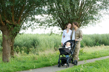Young mother and father walking outdoors with baby in pram