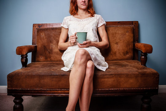 Young woman in summer dress sitting on old sofa drinking tea