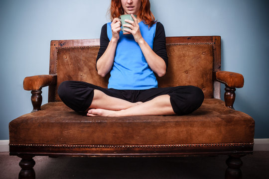 Young woman in relaxed pose is drinking tea on old sofa