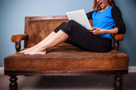 Happy young woman sitting on sofa using her laptop