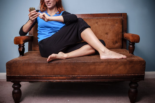 Happy young woman sitting on old sofa using her phone