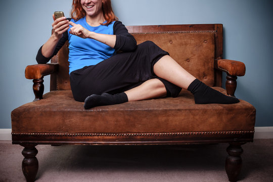 Happy young woman sitting on old sofa using her phone