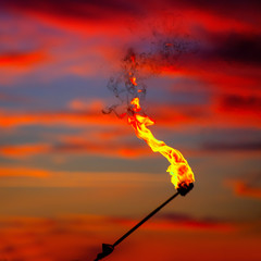 Fire torch at sunset sky with red clouds
