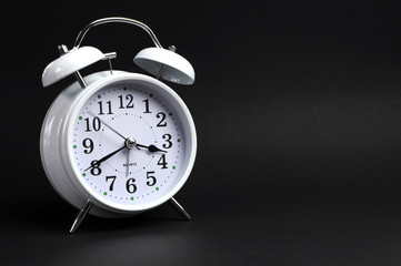 White vintage alarm clock against black background