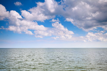 Naklejka na ściany i meble Cloudy blue sky above a surface of the sea