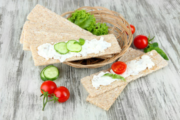 Tasty crispbreads with vegetables on wooden background
