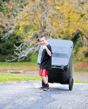 Young boy bringing trash can up the driveway