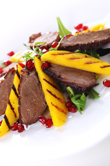 Salad with duck fillet and grilled mango on white background.