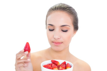 Content brunette woman holding up a strawberry with closed eyes