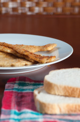 Breaded chicken steaks in a plate, bread and napkin in the table
