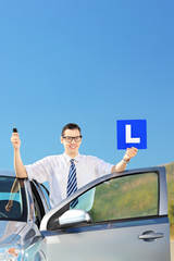 Naklejka na ściany i meble Happy man posing near his car, holding L sign and key on a road