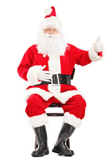 Happy Santa claus sitting on a chair and giving a thumb up