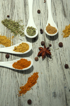 Assortment of spices in  white spoons, on wooden background