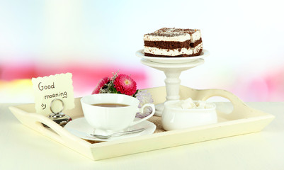 Cup of tea with cakes on wooden tray on table in room