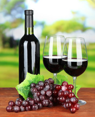 Obraz premium Ripe grapes, bottle and glasses of wine on bright background