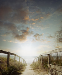 Beautiful moody scene of walkway to beach and sunrise in sky at morning