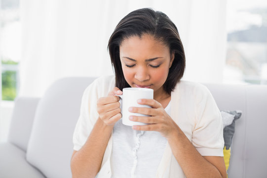 Peaceful young dark haired woman in white clothes enjoying coffe
