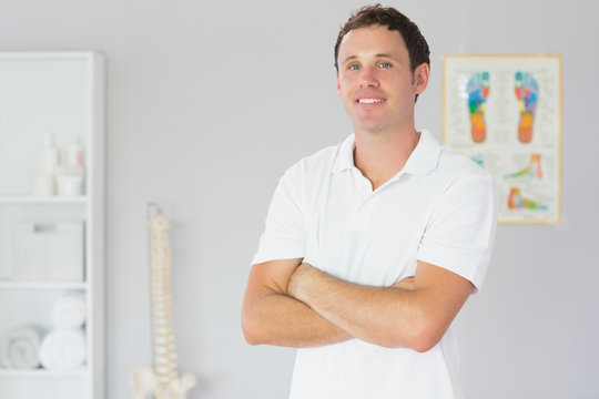 Handsome happy physiotherapist standing with arms crossed