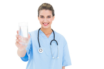 Content brown haired nurse in blue scrubs holding a glass of wat