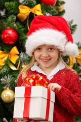 Happy little girl  with gift box near the Christmas tree
