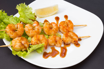 Shrimp shashlik on white plate with sauce and salad
