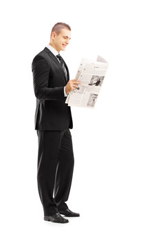 Full length portrait of a young businessman reading a newspaper