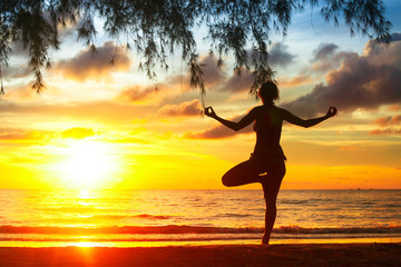 Silhouette of young woman practicing yoga on the beach.